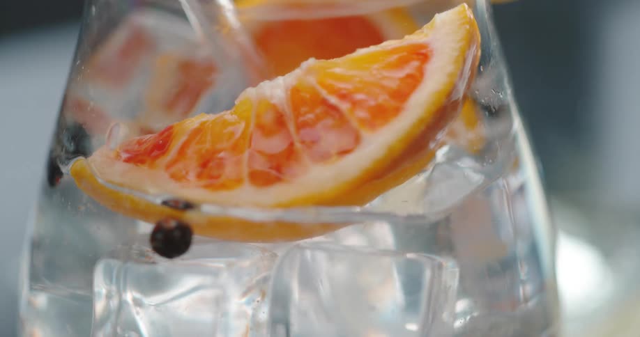 Ice cubes orange slices and water are poured into a glass