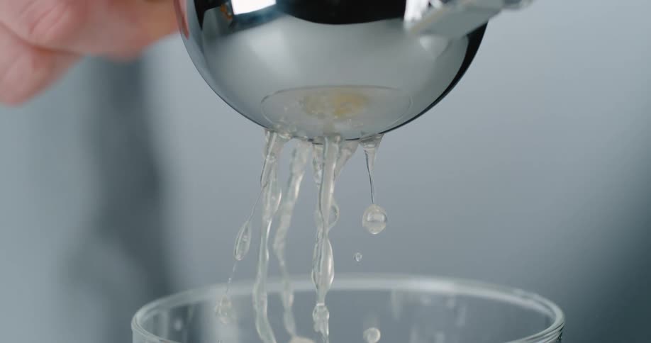 A person is using a presser to strain into a glass