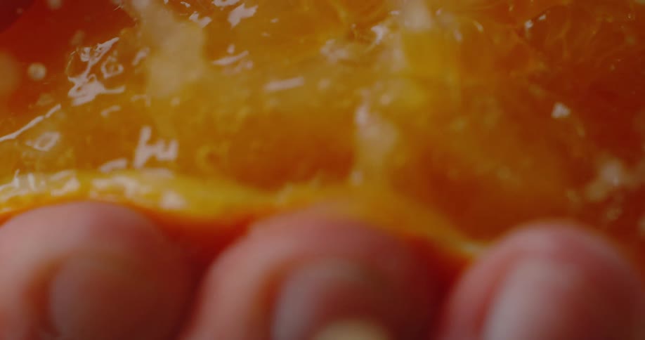 Juice goes flying as a hand squeezes a round orange slice