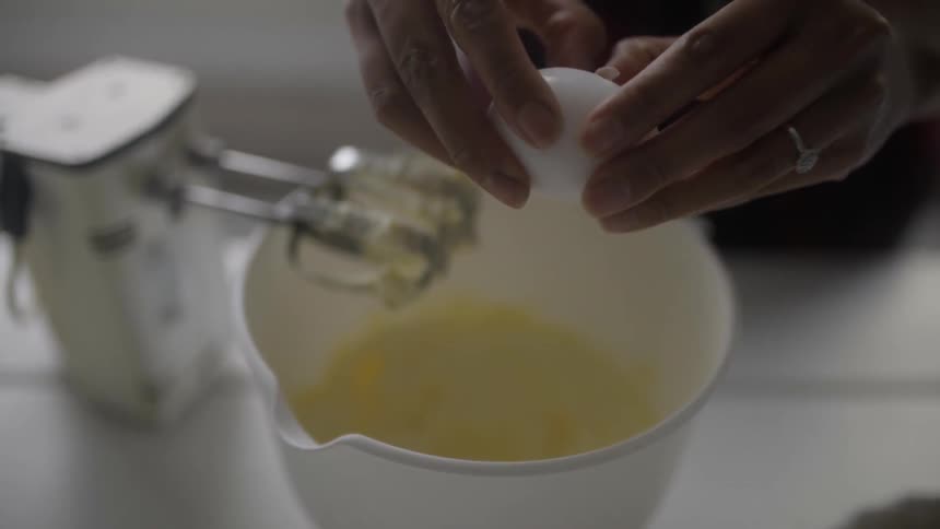 A woman cracks on egg into a mixing bowl