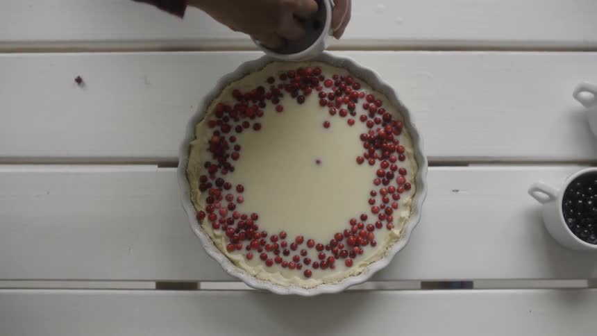 A person puts berries on a custard dessert