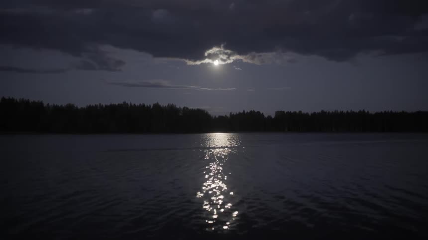 Clouds cover a moon shining on a lake