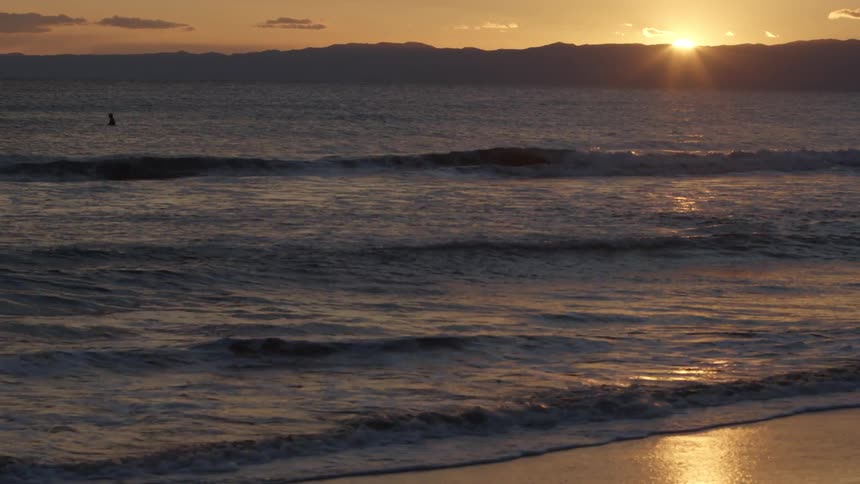A person standing on the shallow ocean water near the beach at sunset
