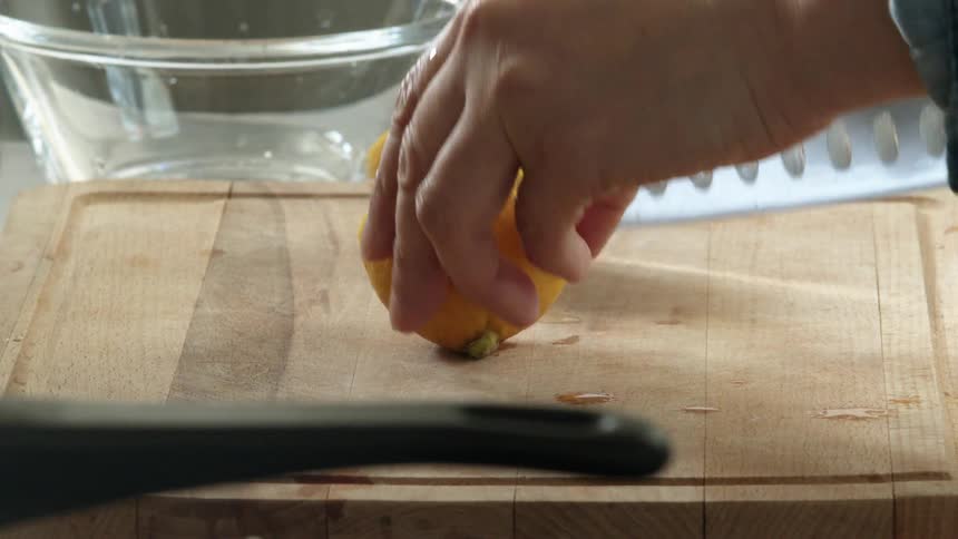 A person uses a knife to slice a lemon in half on a wooden cutting board