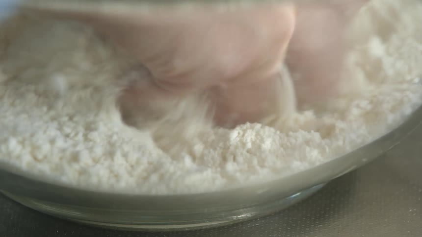 A person is breaking up powder in a bowl with their hand