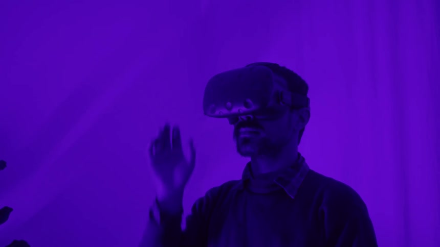 A man wearing a vr headset standing and moving his hand in arranging motion in a room with a purple light