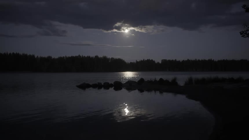 The moon peeks through clouds and reflects in a lake