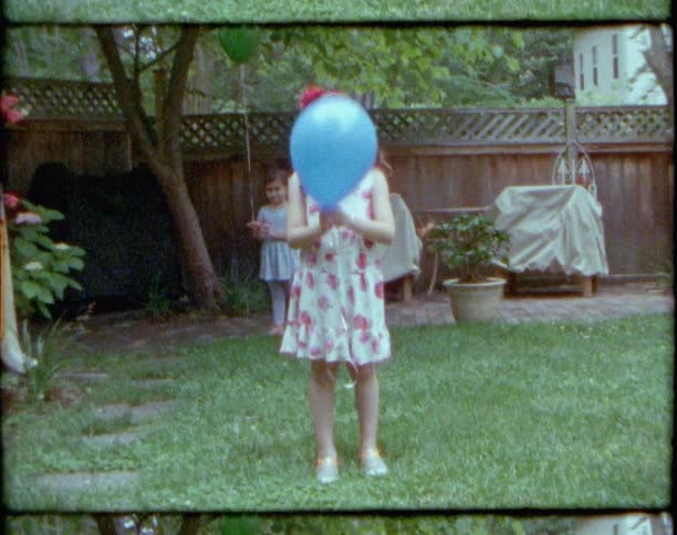 Young girl wearing a dress holds a blue baloon standing on the green grass in the backyard