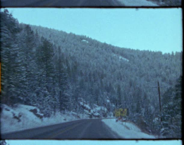 Driving on a road through the pine tree forest covered mountains at winter