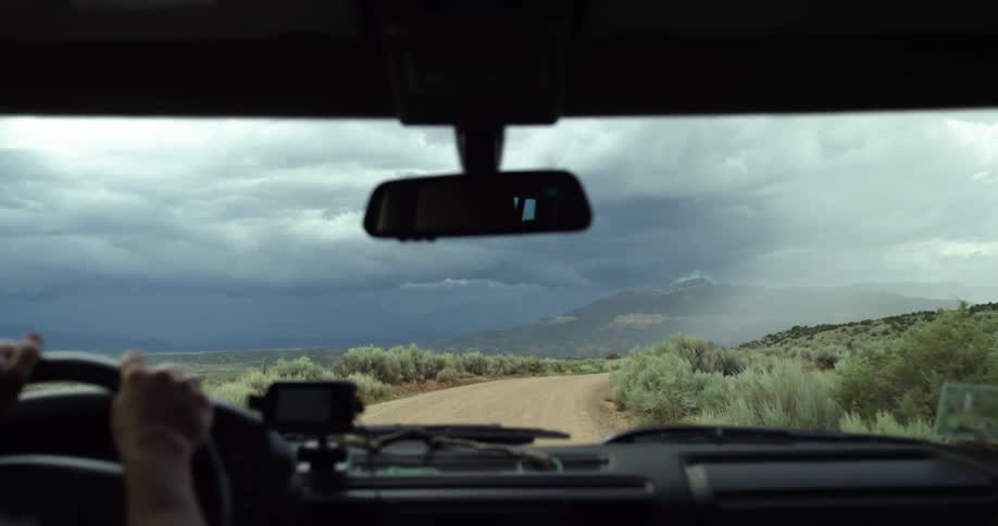 A man driving a car over a dirt road through the shrub land in an overcast day