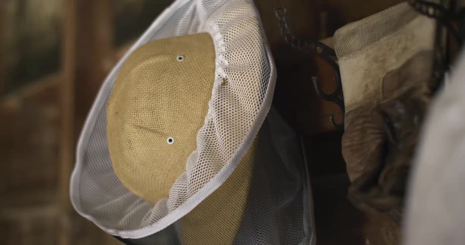 A beekeeper hat and veil hanging from a coat hanger on a wooden wall