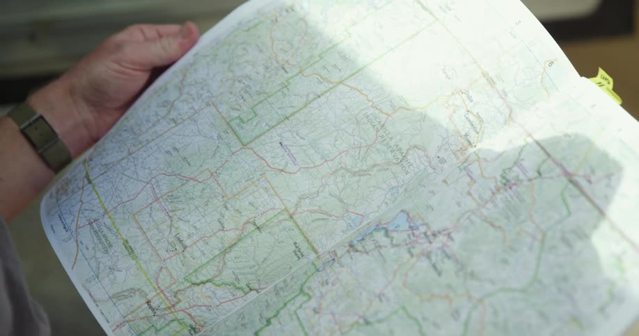 A man flips through the pages of a road map while standing outdoors during the day