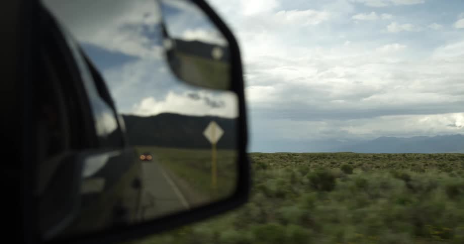 Close up of the rearview mirror reflecting a car driving behind on a rural road