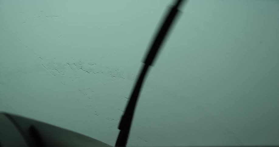 Rain falls on a car window shield while the windshield wipers move back and forth