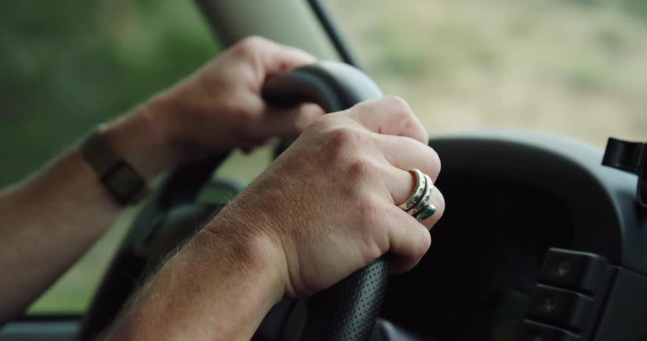 Person wearing ring steers vehicle past hills and shrubs