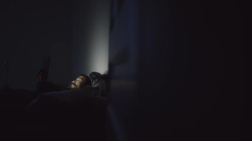 A man is laying in bed indoors and looking at a cellphone