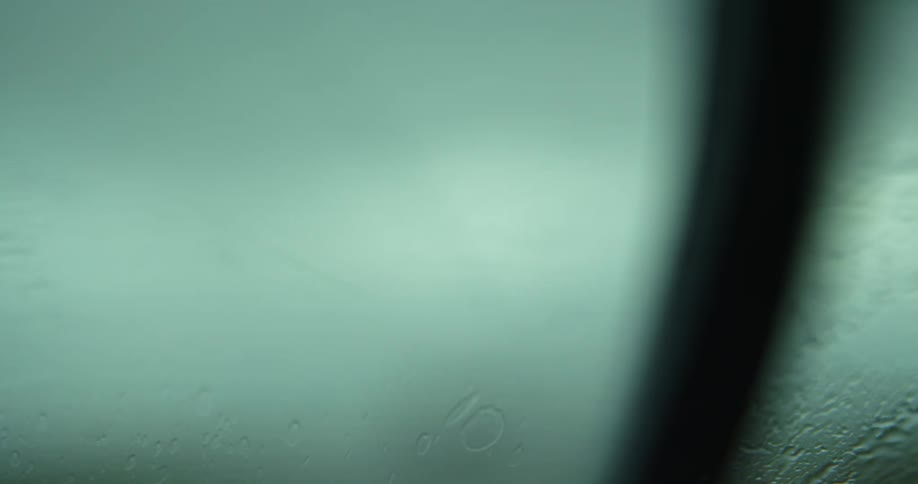 A vehicle with windshield wipers with rain falling on the windshield