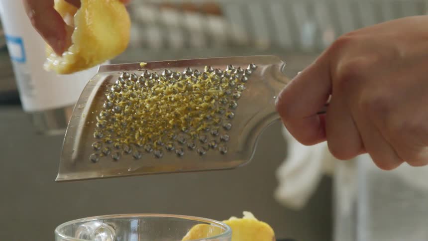 A person grating and orange peel over a glass in a sink