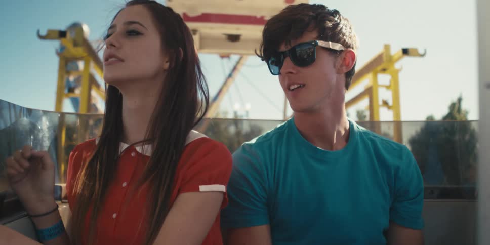 A young woman and man sit together in a carriage of a ferris wheel as it rises into the air during the day