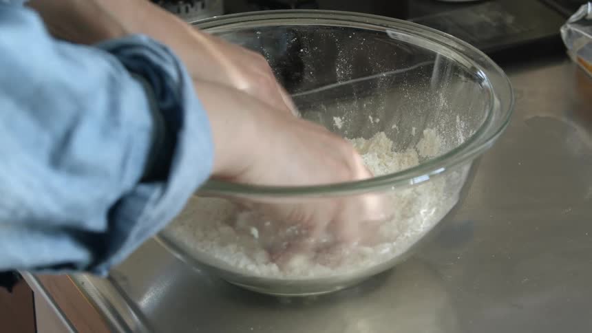 Man mixing flour inside a glass bowl over the kitchen counter top with his hands