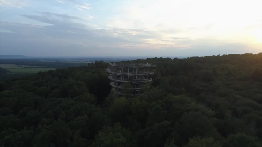 An aerial view of a tall spiral structure surrounded by trees at dawn