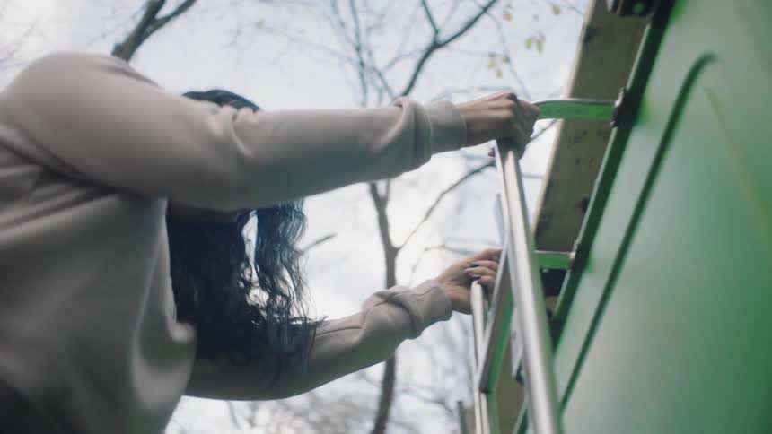A woman climbing down a ladder on a vehicle with trees the sky and clouds in the background