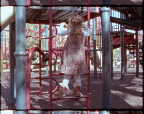 Small blonde girl wearing a dress runs and climbs a playground in a park