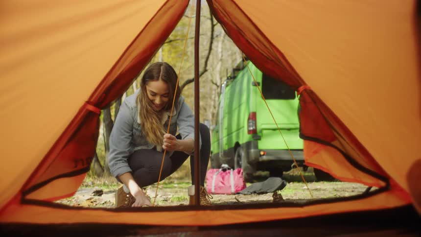 Young woman burying a tent peg using a rock while camping in the forest