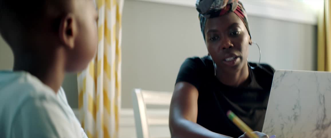 A woman sitting at home with her laptop helps her son with school work