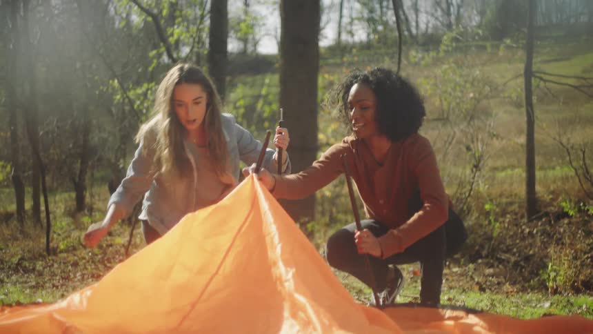 Two girls attempting to build a tent in the woods