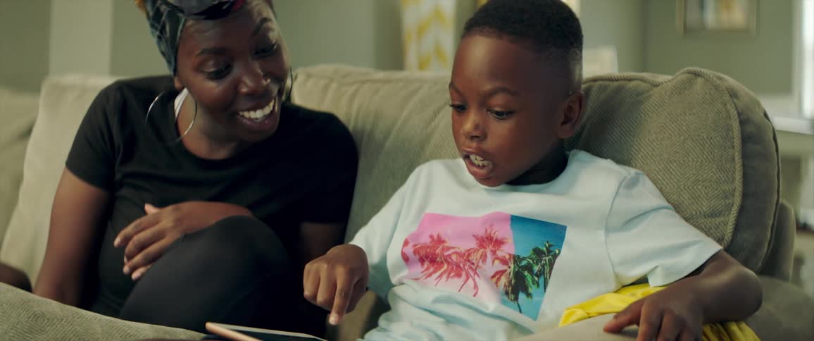 A mother and son smiling while using a tablet on a living room sofa