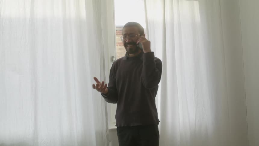 Asian man talking on cell phone with hand gestures near a window