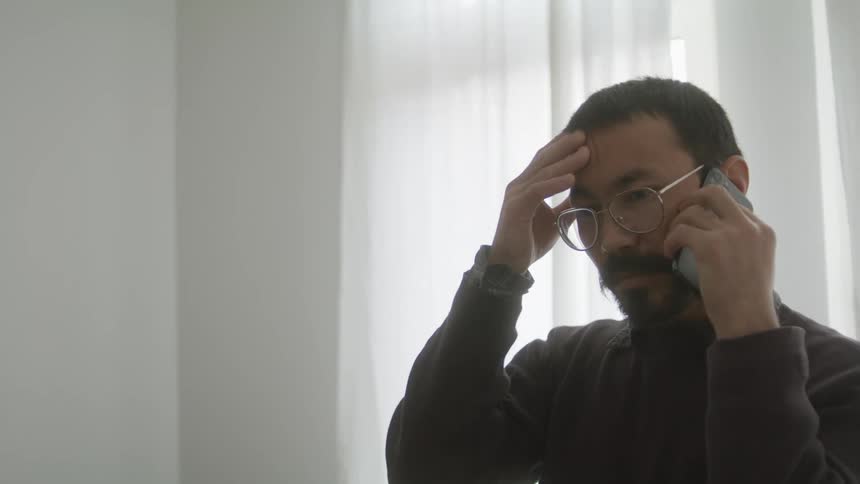 Man listening to phone strokes his forehead