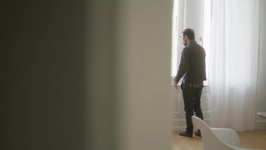 Man with glasses and beard talks on smartphone and walks around in room