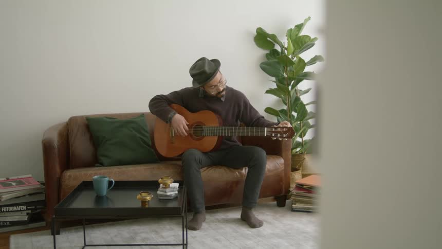 A man is sitting on the couch and playing guitar