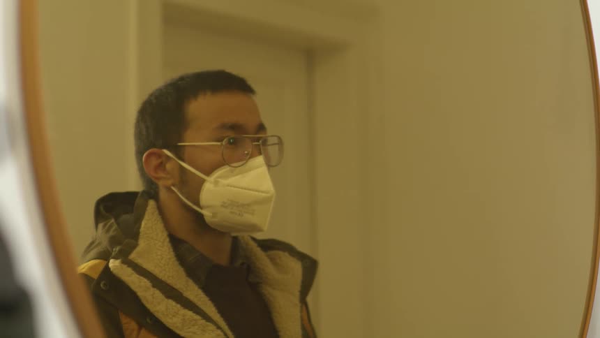 Young bearded man wearing glasses puts a face mask in front of a mirror in the hallway before going out of the house
