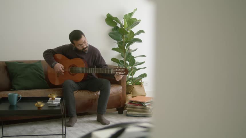 A man is playing guitar while sitting in a room