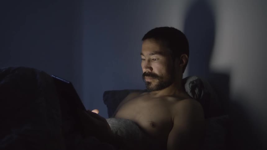 A man lies in bed and types on his tablet