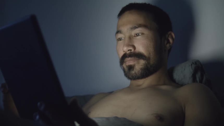 A man sits in bed and looks at his tablet