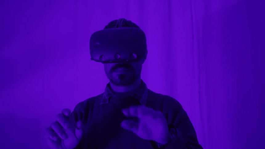 Man wearing virtual reality goggles gesticulates in the air inside a room flooded with magenta lights