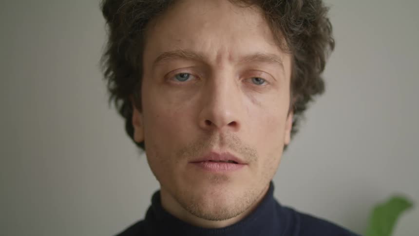 Blue eyed man next to pale interior wall licks lip