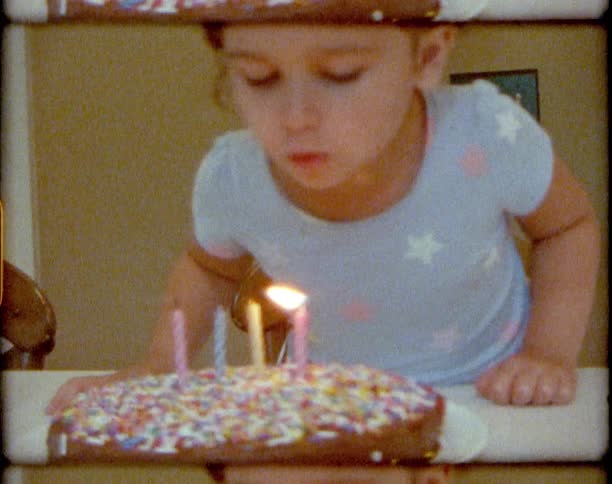 Vintage footage of a little girl blowing out candles on a birthday cake