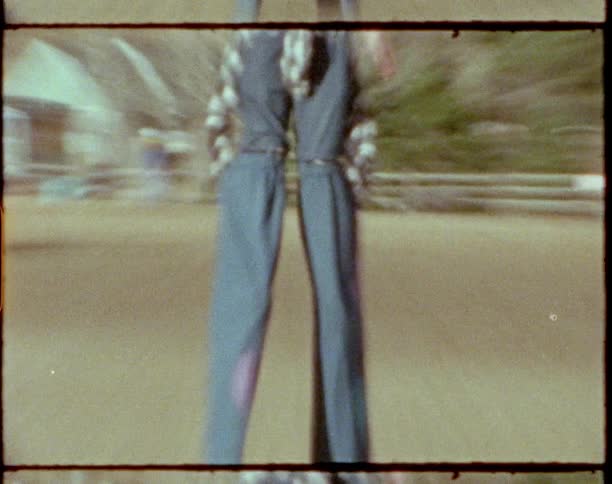 Female wearing hat and overalls trying to walk on stilts