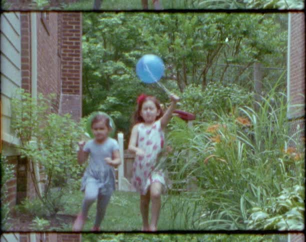 Vintage footage of two little girls carrying balloons running outside a home