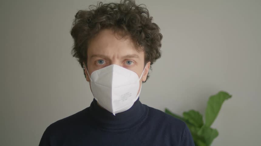A white male looks at the camera while putting on a white face mask
