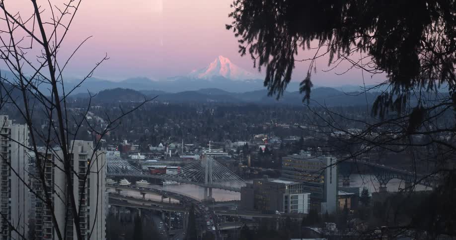 Traffic passes over a river and toward downtown in a city by tall mountain