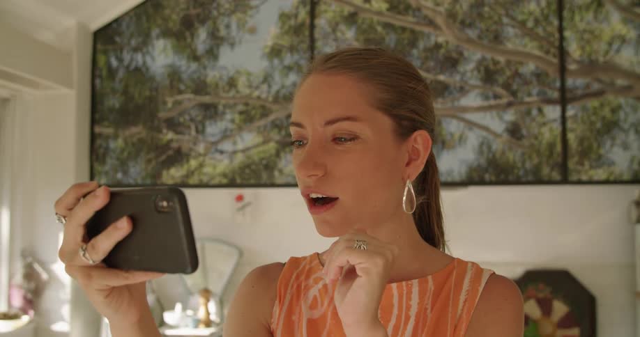 A woman waves to someone during a video call on her smartphone