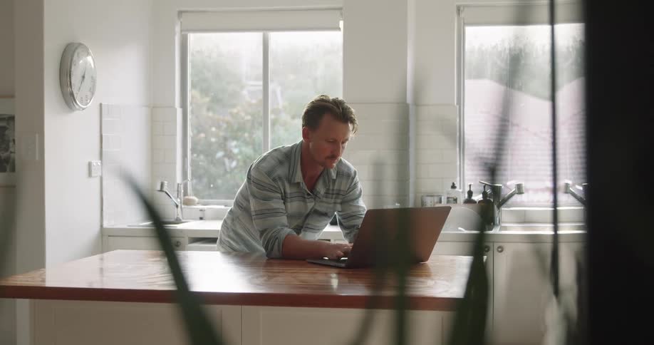 A man is looking at a laptop while standing in his kitchen