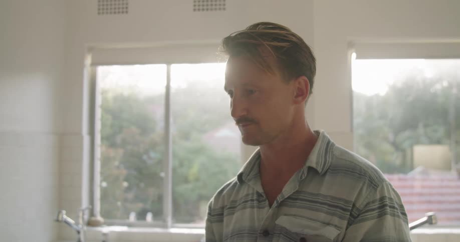 Man stands in kitchen smiling backlit by sun shining through window
