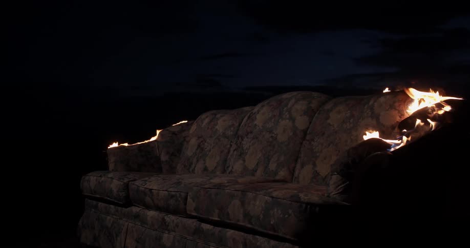 A couch is burning outside at night